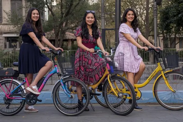 Três mulheres vivendo a estética dorama e mobilidade urbana com bicicletas elétricas e vestidos leves na primavera.