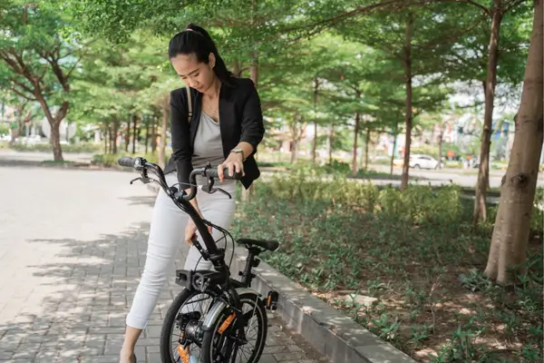 Mulher jovem de blazer preto e calça branca com sua bicicleta elétrica dobrável, inspirada na mobilidade sustentável com charme.